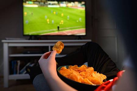 Ein Junge sitzt vor dem Fernseher und ist dabei Kartoffelchips.